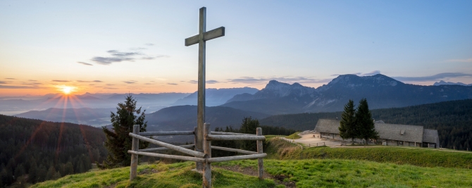 Blick vom Berg mit Gipfelkreuz und Alm