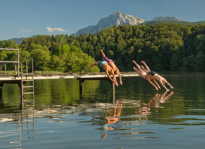 Kinder beim Baden am See mit den Bergen im Hintergrund.