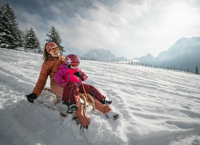 Frau mit kleinem Kind beim Rodeln im Winter.
