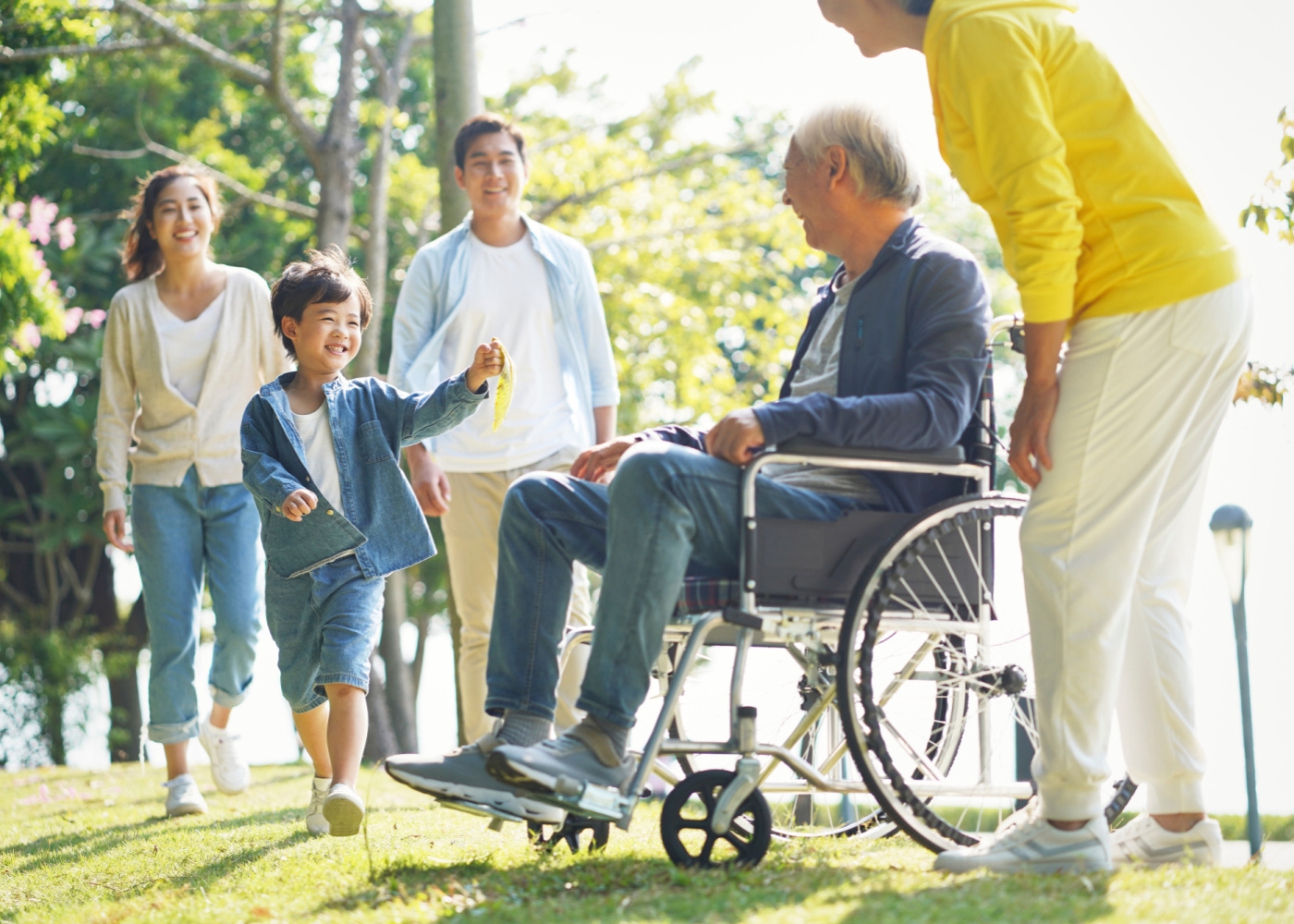 Drei-Generationen-Familie entspannen im Freien, mit Mann im Rollstuhl.